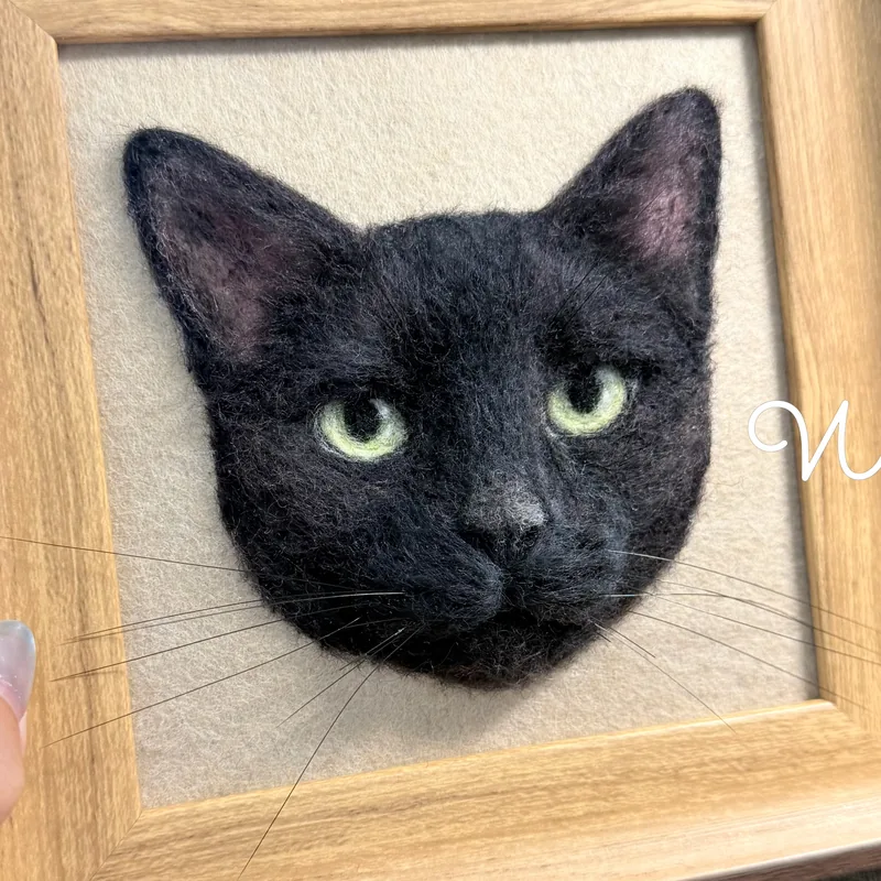 Framed needle felted black cat portrait beside the live cat
